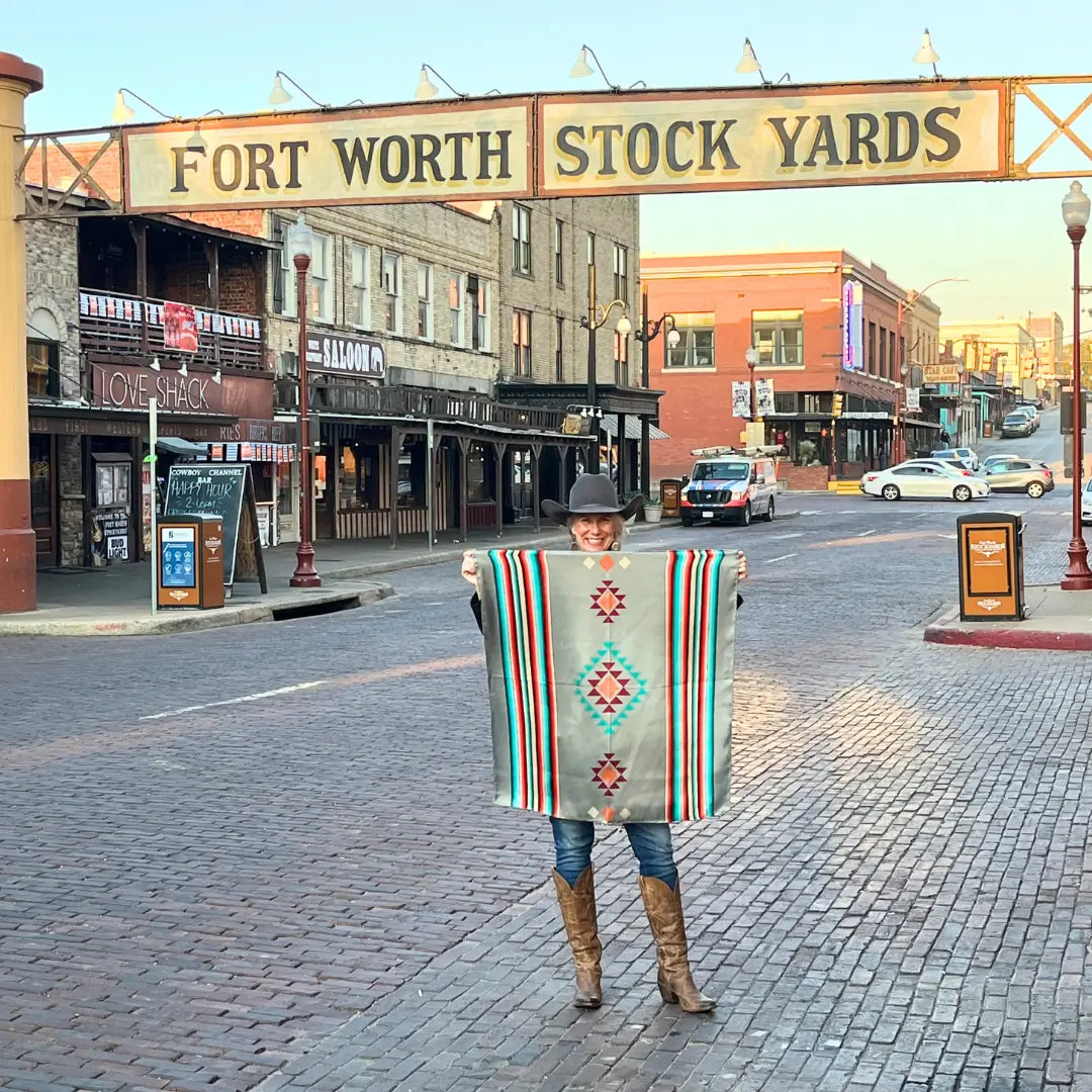 Western Silk Scarf- Cowgirl holding a Cowtown Wild Rags gray serape silk scarf with turquoise, maroon, and coral in the Fort Worth Stockyards.
