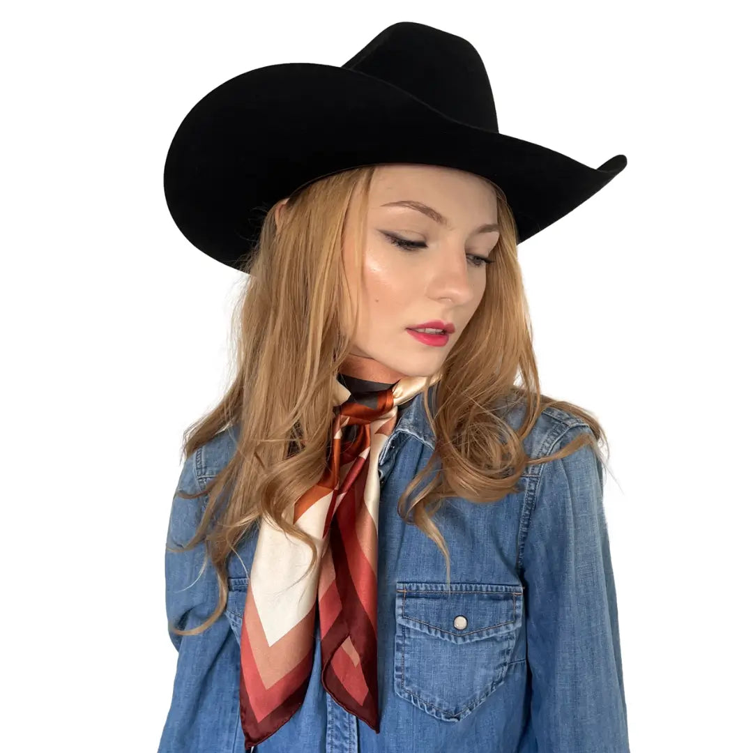 A cowgirl wearing a large Aztec design silk scarf with soft tan, maroon, copper, dusty pink, and charcoal gray.