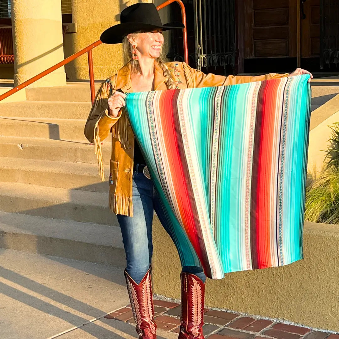 Cowgirl holding a Cowtown Wild Rags turquoise serape silk scarf with blue, tan, maroon, orange and, coral.