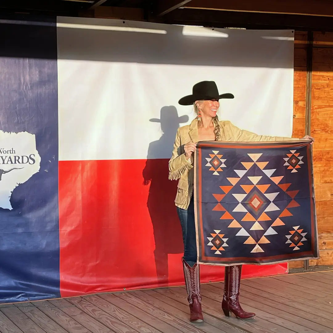 Cowgirl holding a Cowtown Wild Rags Aztec silk scarf with navy blue, soft tan, copper, and charcoal gray in the Fort Worth Stockyards.