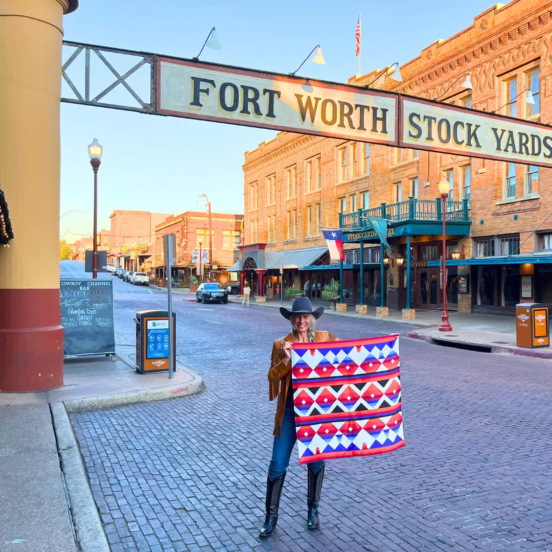 Cowtown Wild Rags - Aztec Red, Blue, Orange Silk Scarf for Men and Women - Cowgirl under the Fort Worth Stockyards sign holding a Cowtown Wild Rags scarf.