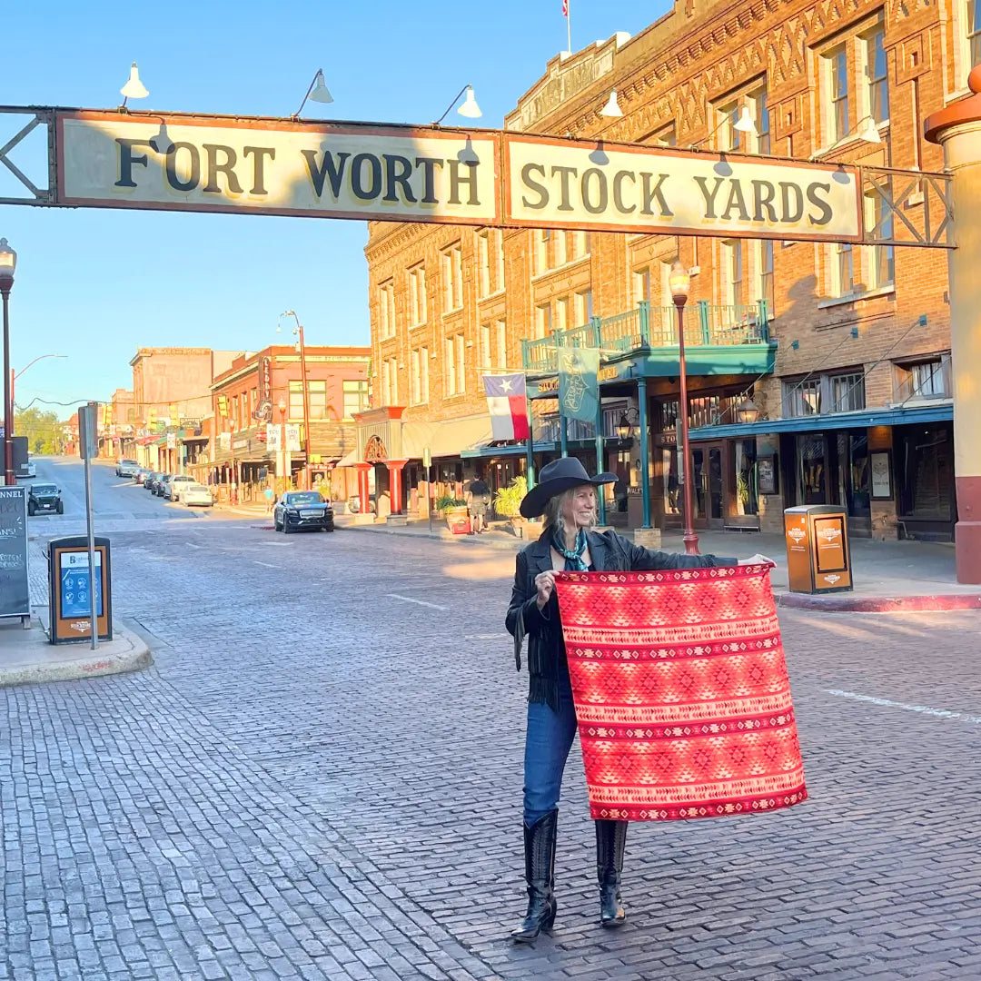 A cowgirl holding an Aztec wild rag silk scarf with red, maroon, copper and peach in the Fort Worth Stockyards.